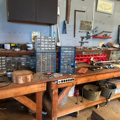 Sale Photo Thumbnail #749: Large wooden workbench loaded with hardware storage drawers, hand tools, framing squares, and various workshop supplies.