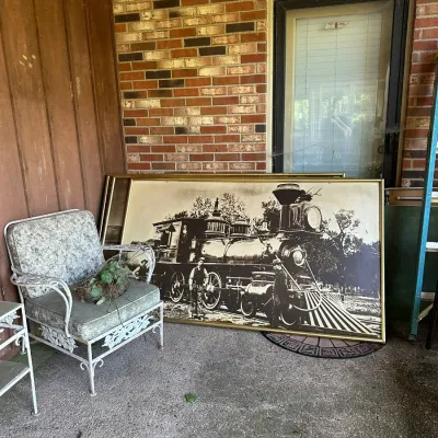 Sale Photo Thumbnail #184: Large vintage framed black-and-white photograph print of a steam locomotive, set on a porch alongside a vintage wrought iron armchair with cushioned seat.