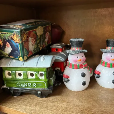 Sale Photo Thumbnail #303: Collection of holiday decorations on a wooden shelf, including ceramic Christmas train cars and painted snowman figurines.