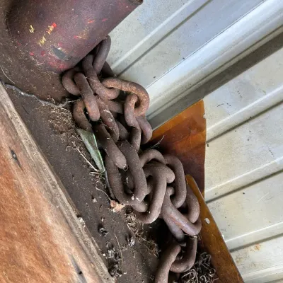 Sale Photo Thumbnail #475: Heavy rusted steel link chain alongside a smaller chain segment and a weathered red metal can, shown on a dusty shelf in aged condition.