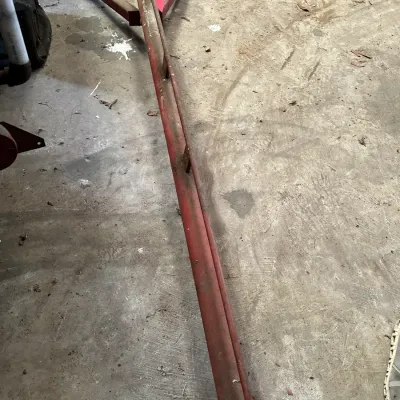Sale Photo Thumbnail #212: Vintage red metal farm implement or tow bar attachment lying on a workshop concrete floor.