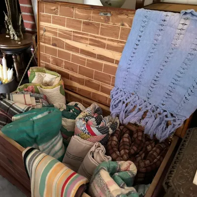 Sale Photo Thumbnail #362: Open cedar storage chest filled with vintage textiles, including handmade quilts, wool blankets, and a light blue woven fringed throw.