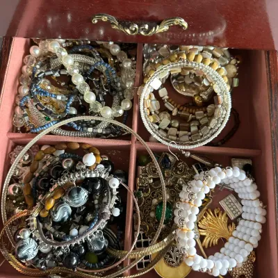 Sale Photo Thumbnail #143: Assortment of costume jewelry, including beaded bracelets, metal chains, and brooches, organized in a felt-lined wooden jewelry box drawer.