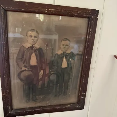 Sale Photo Thumbnail #246: Antique hand-tinted portrait of two young boys in Victorian attire, housed in a distressed dark wooden frame.