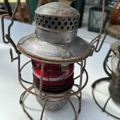 Sale Photo Thumbnail #164: Vintage Dietz Kero railroad lantern featuring a metal wire frame guard and a ruby red glass globe, displaying age-appropriate patina and rust.