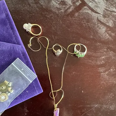 Sale Photo Thumbnail #137: Collection of fine and costume jewelry, including rings with pearl, green, and clear stones, and a gold-tone snake chain necklace with a purple pendant.