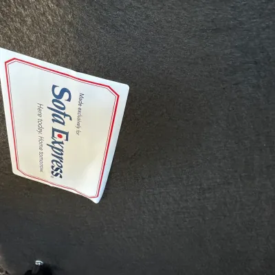 Sale Photo Thumbnail #373: Manufacturer tag for Sofa Express attached to the black dust-cover underside of a piece of upholstered furniture.