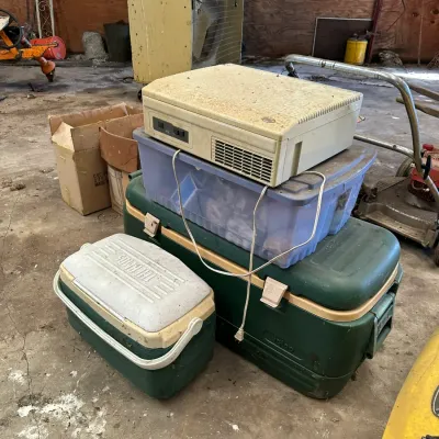 Sale Photo Thumbnail #548: Collection of vintage plastic coolers including Thermos and Igloo brands, alongside a clear storage tote and a vintage desktop computer chassis in a workshop.