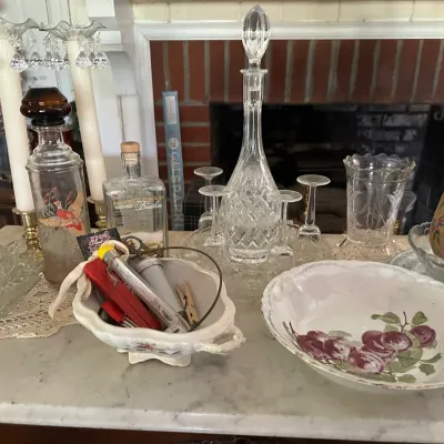 Sale Photo Thumbnail #653: An assortment of vintage glassware and home decor, including crystal decanters, stemware, a fruit-patterned serving bowl, glass candelabras, and painted wooden clogs.