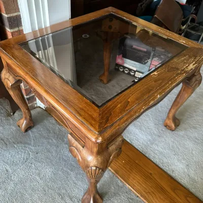 Sale Photo Thumbnail #451: Square wooden side table with a inset glass top, carved cabriole legs, and ball-and-claw feet. The wooden finish shows significant wear and scuffing along the edges.