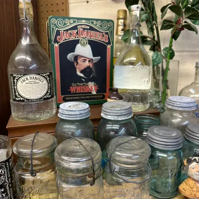 Sale Photo Thumbnail #30: Collection of vintage glassware and collectibles, including wire-bail Ball Ideal mason jars, zinc-top canning jars, Jack Daniel's spring water bottles, and a decorative tin.