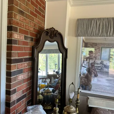 Sale Photo Thumbnail #197: Traditional dark wood wall mirror featuring a carved ornate crest, shown alongside brass table lamps.