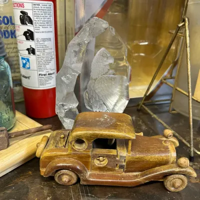 Sale Photo Thumbnail #31: Handcrafted wooden vintage model car displayed alongside an etched glass eagle paperweight and household bar items.