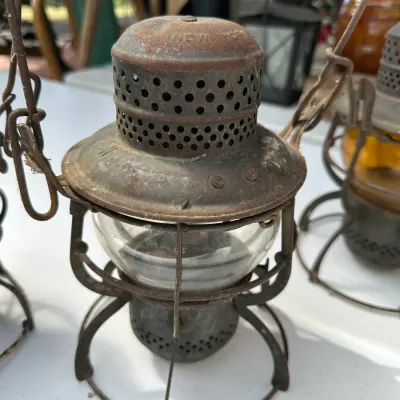 Sale Photo Thumbnail #165: Antique railroad style metal oil lantern featuring a clear glass globe, perforated chimney, and rusted wire cage frame.