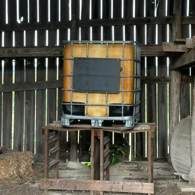 Sale Photo Thumbnail #326: Large industrial IBC tote container in a metal cage, elevated on a rustic wooden stand inside a barn structure.