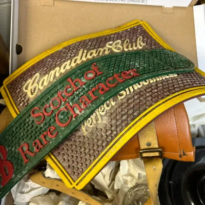 Sale Photo Thumbnail #36: Vintage rubber bar spill mats, including Canadian Club and Scotch of Rare Character branded designs, shown resting inside a cardboard box.
