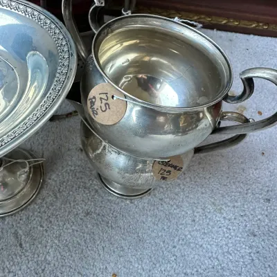 Sale Photo Thumbnail #401: Vintage silver-plated creamer and sugar bowl set alongside a silver-plated pedestal dish, displaying minor surface tarnish.