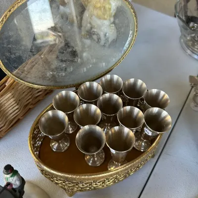 Sale Photo Thumbnail #399: Vintage gold-toned filigree mirrored caddy holding a set of small silver-toned cordials or shot glasses.