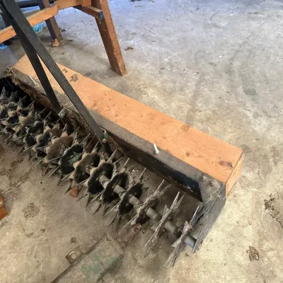 Sale Photo Thumbnail #218: Heavy-duty tow-behind lawn aerator attachment with star-shaped spike wheels and a wooden weight tray.