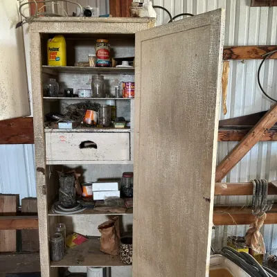 Sale Photo Thumbnail #736: Vintage tall wooden storage cabinet with a heavily distressed, crackled white finish, filled with various workshop tools, jars, and supplies.