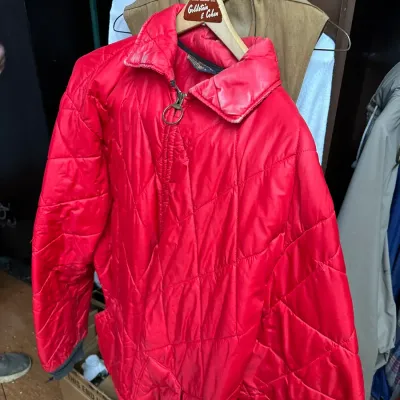 Sale Photo Thumbnail #85: Vintage red quilted jacket featuring a half-zip closure with a ring pull, hanging on a wooden Goldstein & Cohen hanger alongside additional vintage outerwear.