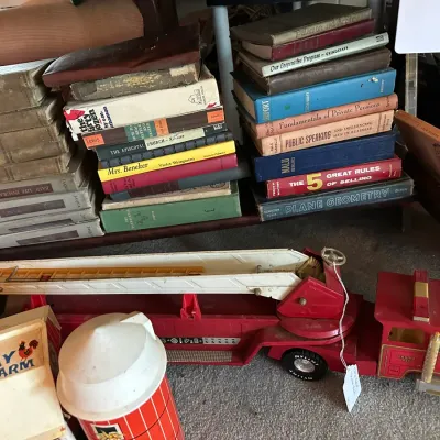 Sale Photo Thumbnail #189: Vintage pressed steel Nylint fire ladder truck displayed below shelves filled with stacks of old hardcover books. The collection includes vintage Fisher-Price Play Family Farm toys nearby.