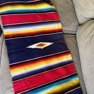 Sale Photo Thumbnail #626: Mexican Saltillo sarape runner featuring vibrant multicolored stripes, a central diamond motif, and fringe detailing along the edges.