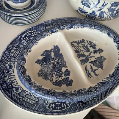 Sale Photo Thumbnail #695: Vintage Blue Willow pattern dishware collection, featuring a divided serving dish, oval platter, stack of saucers with a teacup, and a tureen.