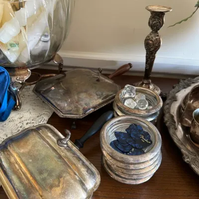 Sale Photo Thumbnail #669: Collection of vintage silver-plated tabletop items, including silent butlers, glass-bottom coasters holding Fender guitar picks, and an ornate candlestick holder.