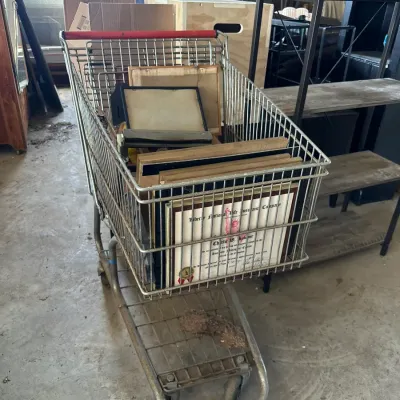 Sale Photo Thumbnail #471: Metal shopping cart filled with various framed pictures, diplomas, and artwork.