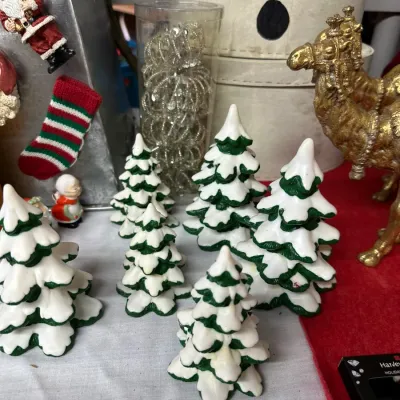 Sale Photo Thumbnail #16: Collection of snowy ceramic Christmas tree figurines arranged with other holiday decor, including golden camel statues and Santa ornaments.