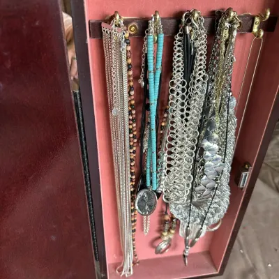 Sale Photo Thumbnail #146: Wooden standing jewelry cabinet filled with various statement necklaces, silver-tone chain mail, and beaded pieces.