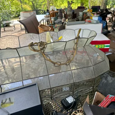 Sale Photo Thumbnail #170: Vintage leaded glass and brass dining light fixture with floral etching, set among various household goods on a patio.