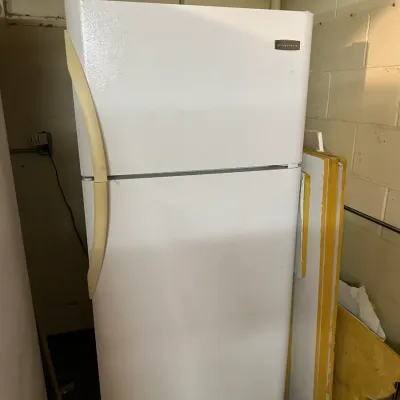 Sale Photo Thumbnail #82: White Frigidaire top-freezer refrigerator featuring curved off-white handles, positioned in a basement or utility space.