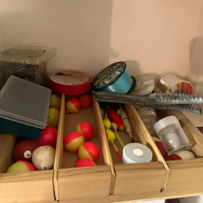 Sale Photo Thumbnail #224: Vintage wooden tray filled with assorted fishing tackle, including red and yellow plastic bobbers, spools of Omniflex fishing line, and metal scaling tools.