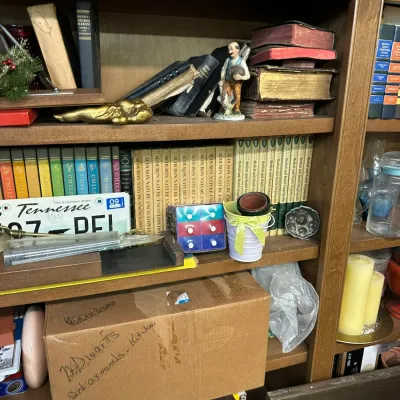 Sale Photo Thumbnail #295: Wooden bookcase filled with vintage encyclopedia sets, old leather-bound books, porcelain figurines, decorative knick-knacks, and a Tennessee license plate.