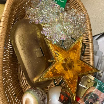 Sale Photo Thumbnail #77: Wicker basket containing vintage Christmas decor, including a gold star tree topper, iridescent snowflake lights, and decorative ball ornaments.