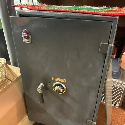 Sale Photo Thumbnail #286: Vintage Mosler heavy-duty steel safe featuring a combination dial and handle mechanism, showing a aged patina and original metal badging.