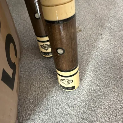 Sale Photo Thumbnail #380: Detail view of the butt ends of vintage Crest brand billiard cues, featuring wood grain sections, cream-colored accents, and circular mother-of-pearl style inlays.