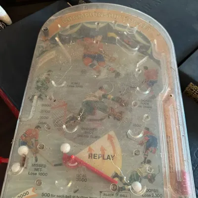 Sale Photo Thumbnail #367: Vintage Championship Hockey handheld bagatelle pinball game with clear plastic casing and hockey player graphics, showing minor surface dust and wear.