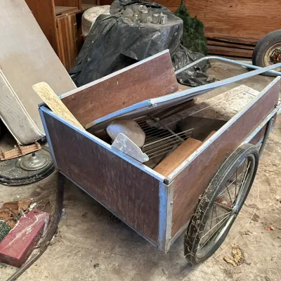Sale Photo Thumbnail #556: Vintage handmade wooden utility garden cart with spoked wheels and aluminum metal trim, showing wear and filled with miscellaneous debris.