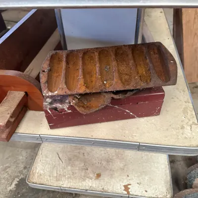 Sale Photo Thumbnail #217: Vintage cast iron cornbread stick pan with significant surface rust, resting on top of a red wooden box.