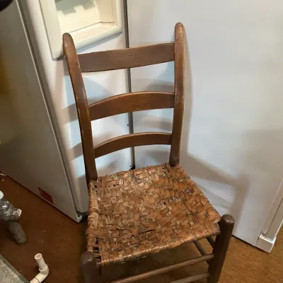Sale Photo Thumbnail #81: Rustic ladderback dining chair featuring a woven split-bark or cane seat and turned wooden legs.