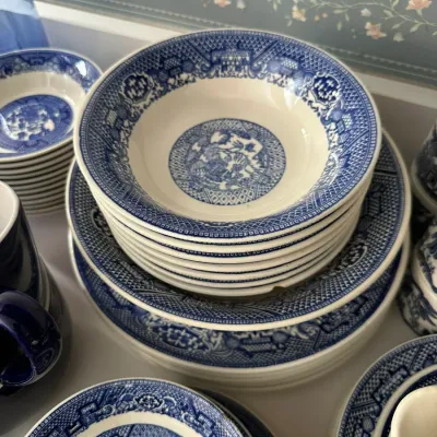 Sale Photo Thumbnail #700: Stack of vintage blue Willow pattern stoneware bowls and plates, displayed alongside matching dishware.