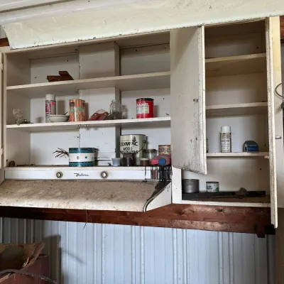 Sale Photo Thumbnail #737: Vintage white painted wooden workshop cabinets with open doors, housing various old paint cans and chemicals above an integrated range hood.