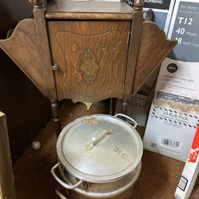 Sale Photo Thumbnail #39: Vintage drop-leaf wooden sewing cabinet with stenciled front panel paired with a large aluminum stock pot sitting below.