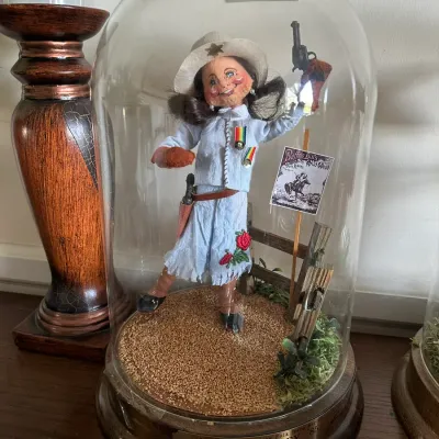 Sale Photo Thumbnail #592: Annalee Doll Society Folk Hero Series "Annie Oakley" collectible doll inside a glass cloche dome, dated 1985.