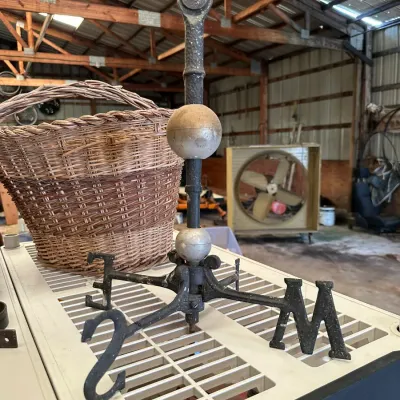 Sale Photo Thumbnail #531: Antique cast iron weather vane base featuring cardinal direction markers and decorative glass lightning rod globes, shown alongside a large woven wicker basket.