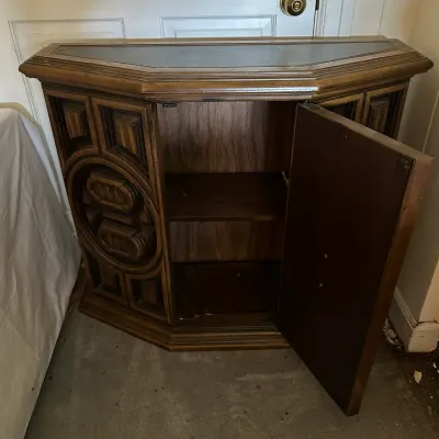 Sale Photo Thumbnail #578: Vintage 1970s brutalist-style wood cabinet featuring ornate geometric relief detailing, a leather-style inset top, and interior shelving.