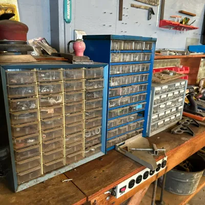 Sale Photo Thumbnail #501: Set of vintage blue metal parts cabinets with clear plastic storage drawers arranged on a wooden workbench.